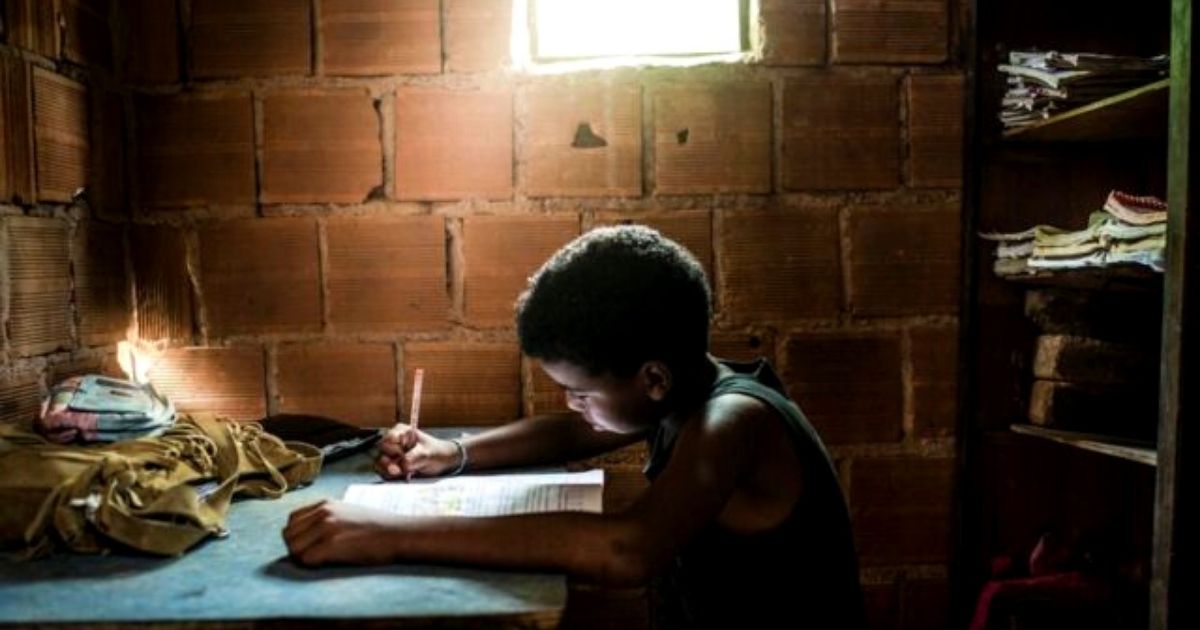 foto mostra menino estudando em uma casa de alvenaria